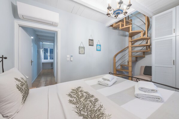 A bedroom with a bed, a wooden spiral staircase, and a view of the hallway.