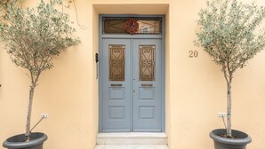 Puerta doble con un adorno de lazo, número 20, flanqueada por dos olivos en macetas.