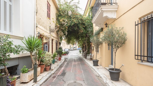Una calle estrecha flanqueada por macetas y edificios con balcones.