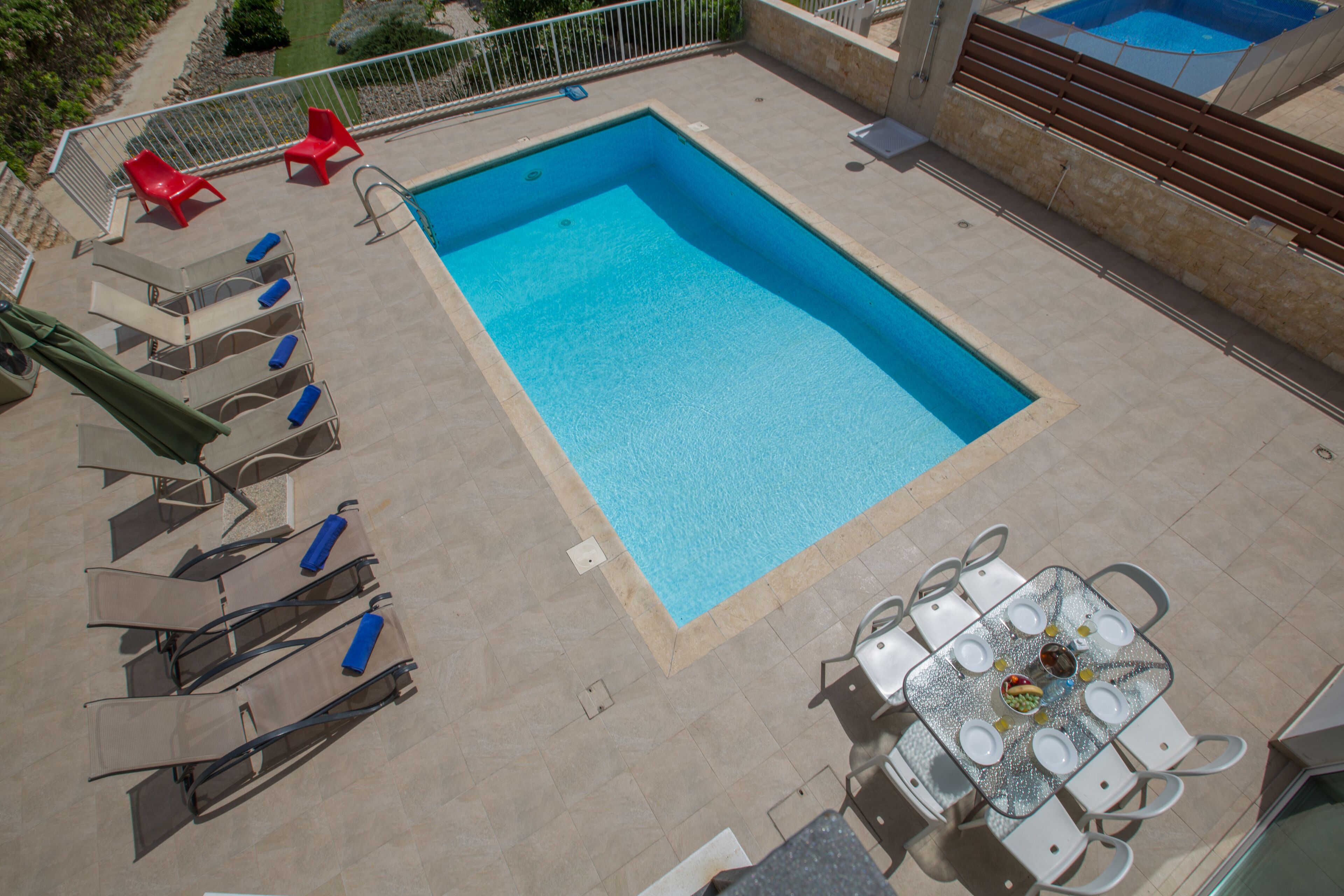 Una piscina rectangular con solárium alicatado, rodeada de tumbonas y una mesa con sillas.