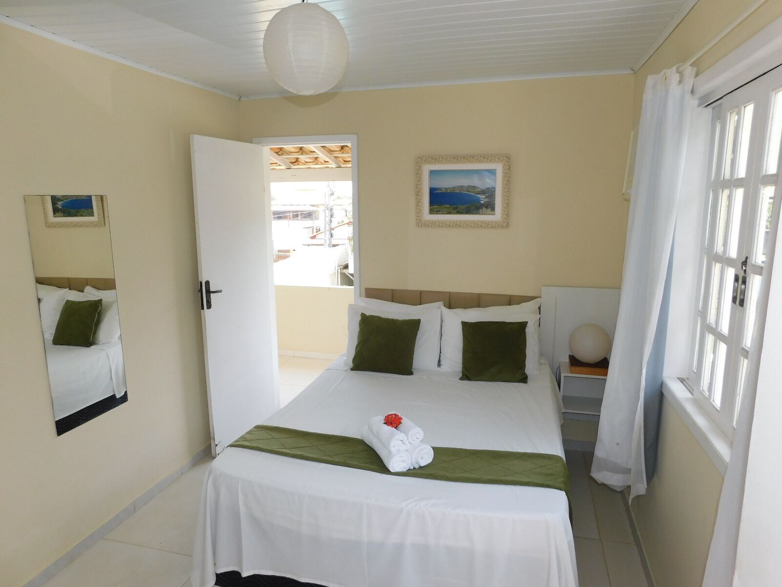 Habitación de hotel con cama, ventana con cortinas, puerta que da al exterior y un cuadro colgado en la pared.
