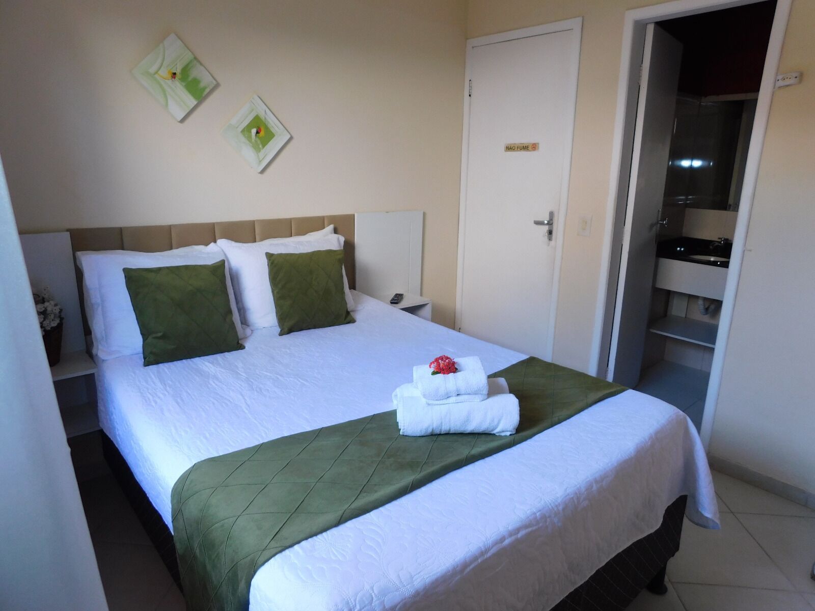 Habitación de hotel con cama, mesita de noche, puerta y baño visible a través de una puerta abierta.