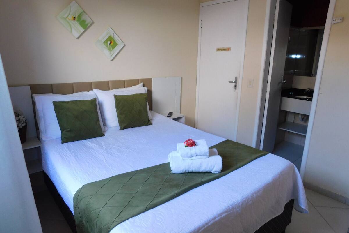 Ein Hotelzimmer mit Bett, Nachttisch, Tür und einem durch eine geöffnete Tür sichtbaren Badezimmer.