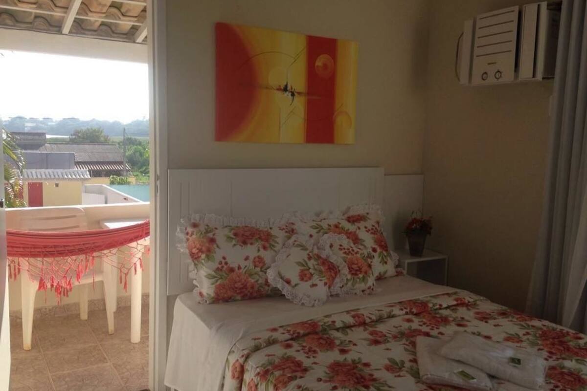 Ein Schlafzimmer mit einem Bett, floralem Bettbezug, einem Gemälde und Blick ins Freie.