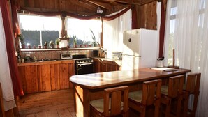 A wooden kitchen with a wooden countertop, a stove, a sink, and a refrigerator. There are potted plants on the windowsill and wooden chairs around the table. - Santa Ana City Views Breathtaking Chalet (Santa Ana)
