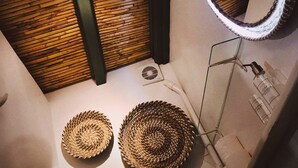 Un baño con techo de listones de madera, un espejo redondo y tres cestas tejidas en el suelo.
