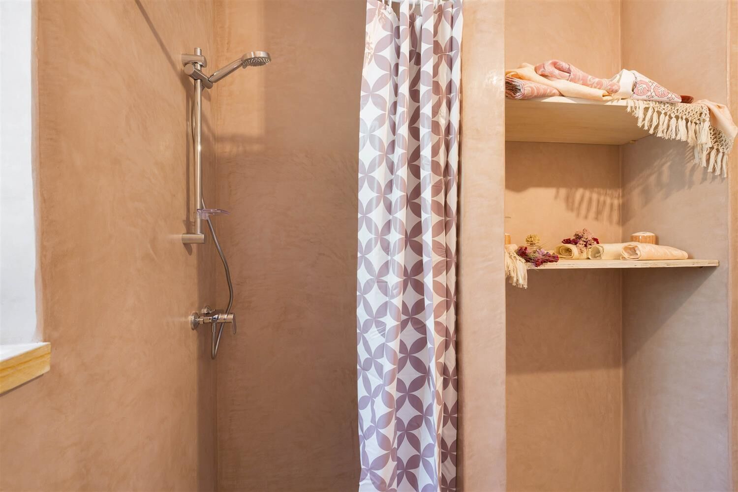Ein Badezimmer mit Dusche, einem gemusterten Vorhang und einem Ablagebereich mit Handtüchern und Pflegeartikeln.