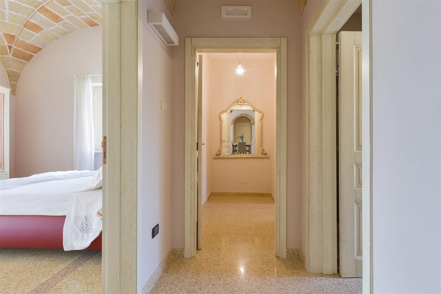 A hotel room with a bed, a bathroom with a mirror, and a hallway leading to another room.