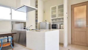 A compact kitchen with white cabinetry, a built-in microwave, and a stainless steel refrigerator. - Ten Apartment Hotel (Fukuoka)