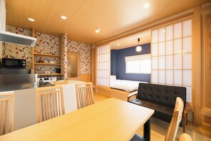 A compact room with a kitchenette, a dining table, a sofa, and a bed with a view of the outside.