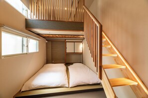 A bedroom with a bed, a window, and a wooden staircase.