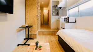 A compact bedroom with a bed, a small kitchenette, a TV, and a wooden floor. - Ten Apartment Hotel (Fukuoka)