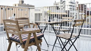 A balcony with wooden chairs and a table, a vase with flowers, and a sign. - Ten Apartment Hotel (Fukuoka)