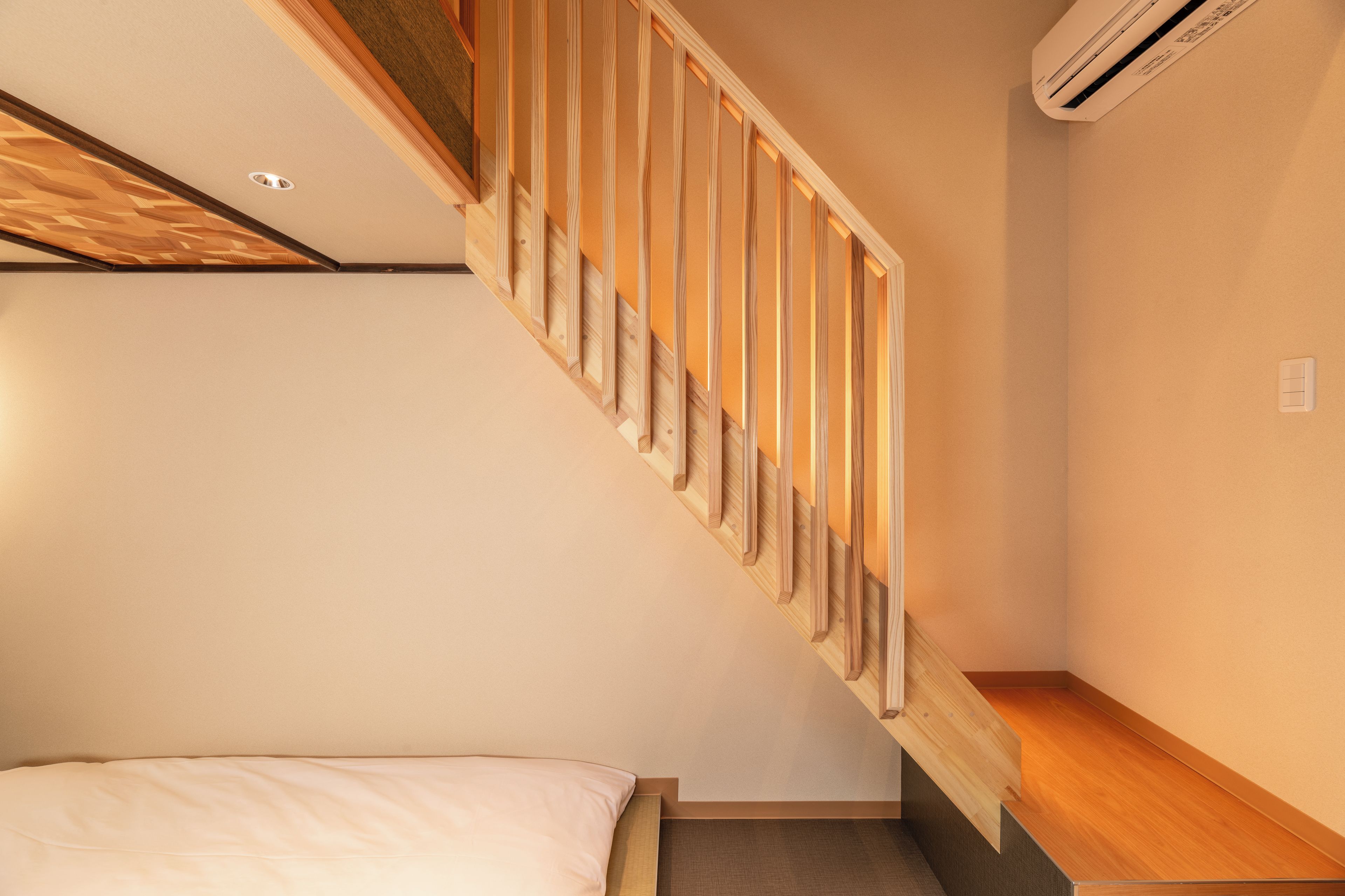 A staircase with wooden steps and a handrail, leading to a bedroom with a bed and a nightstand.