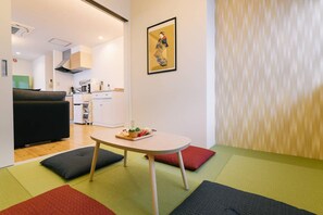 Ein modernes Wohnzimmer mit einer Couch, einem kleinen Tisch mit einer Snackauswahl und einer Küche im Hintergrund.