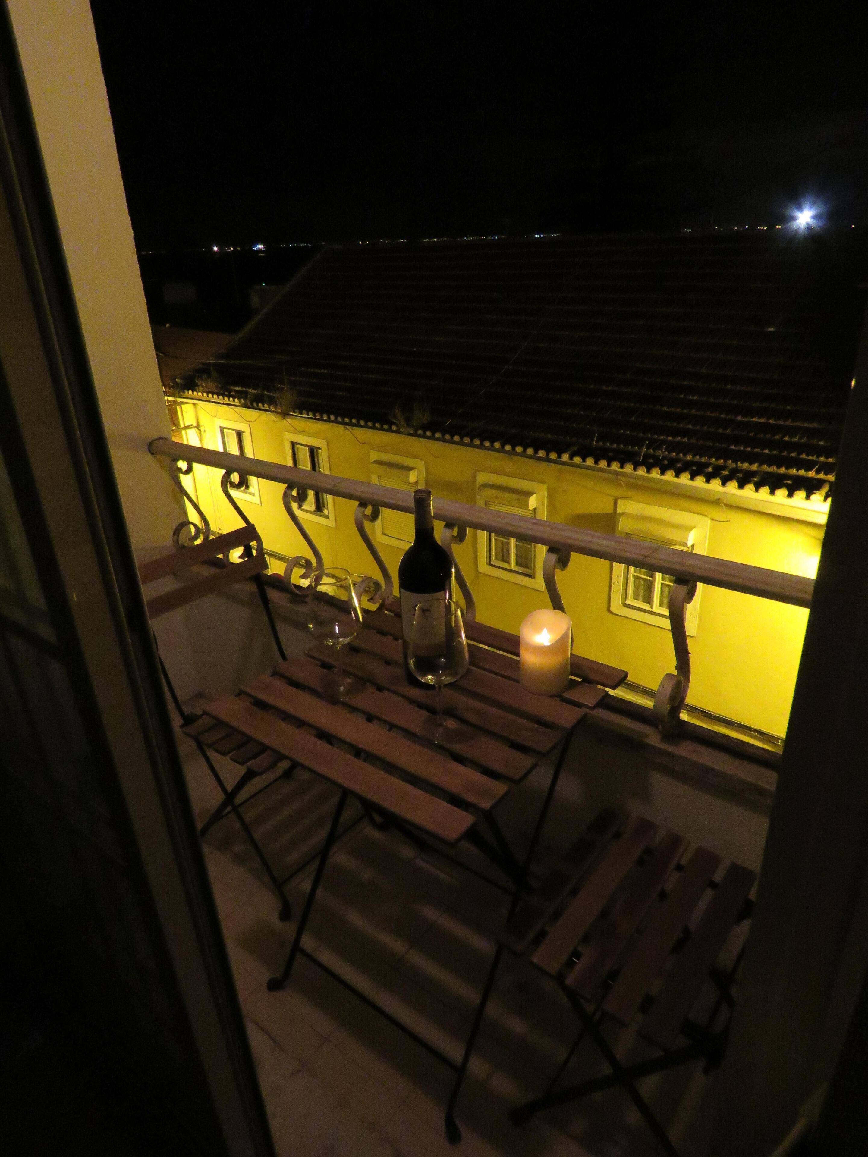Un balcon avec une table, des chaises, une bouteille et une bougie.
