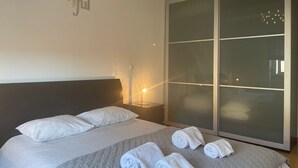 A hotel room with a bed, pillows, a nightstand, a lamp, and a large sliding door. - TEJO HOUSE RIVER Lisbon (Cacilhas) (Almada)