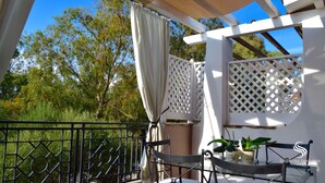 A balcony with a white lattice structure, a black metal railing, and two chairs.