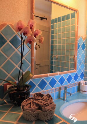 Un baño con un salpicadero de azulejos azules, un lavabo blanco, un espejo y una orquídea en maceta.