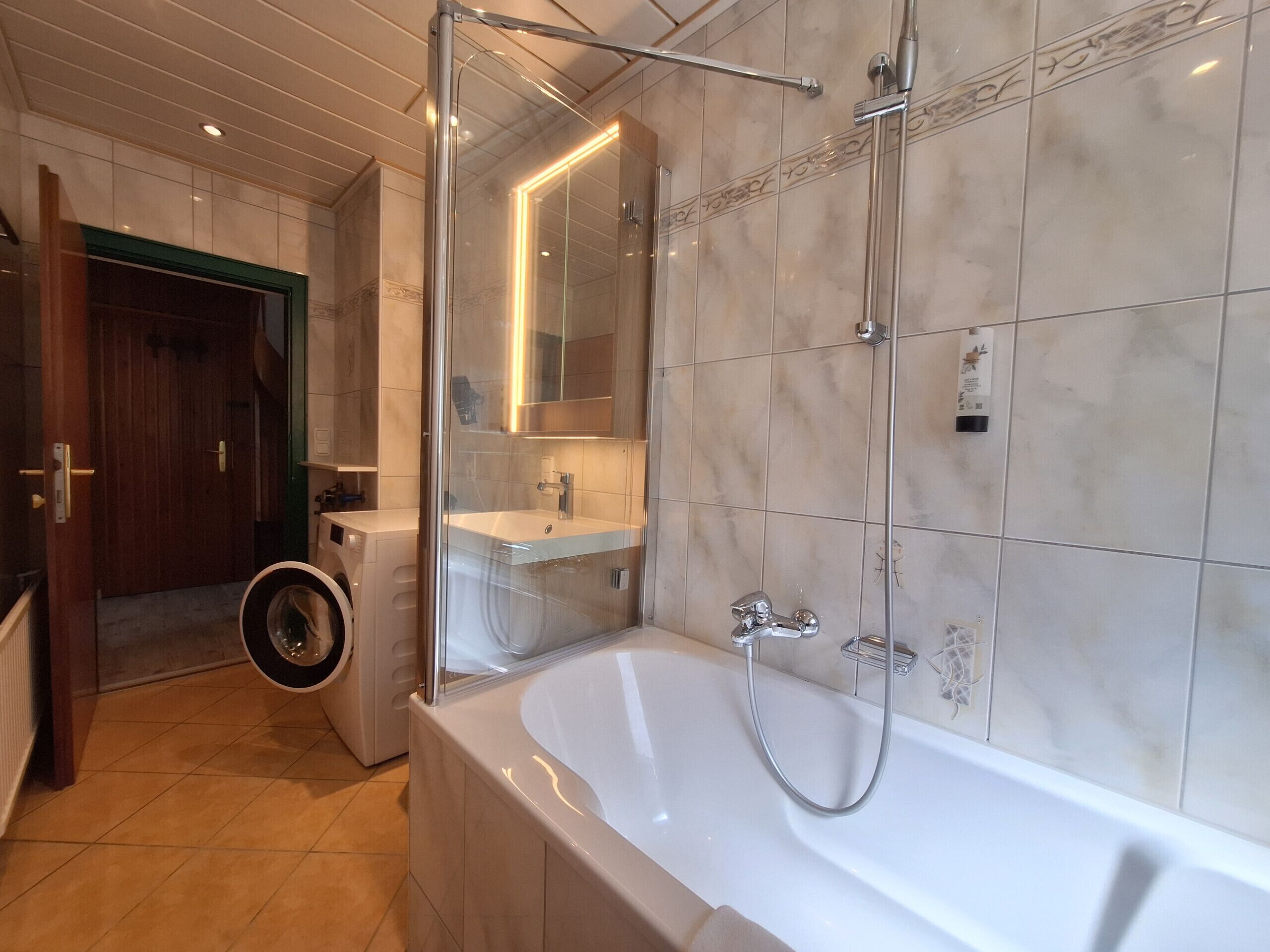 A modern bathroom with a large bathtub, a glass-enclosed shower, and a visible washing machine.