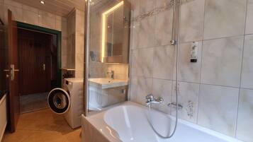 A modern bathroom with a large bathtub, a glass-enclosed shower, and a visible washing machine.