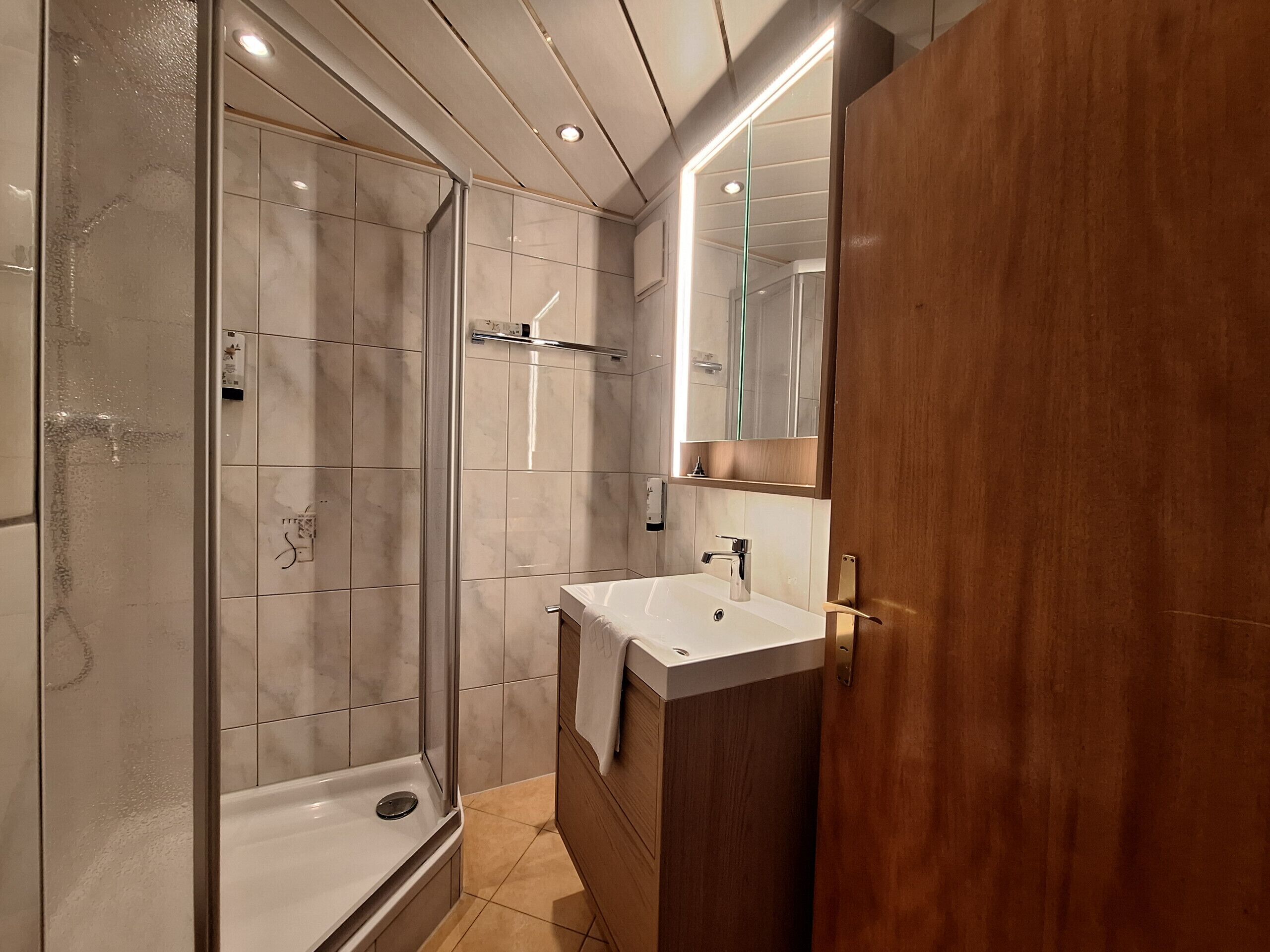 A modern bathroom with a glass shower enclosure, a white sink, and a wooden vanity.