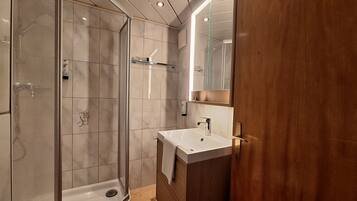 A modern bathroom with a glass shower enclosure, a white sink, and a wooden vanity.