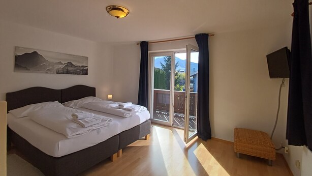 A bedroom with a bed, a painting, a ceiling light, a balcony with a view, and a small table. - The Steinbock Lodge (Zell am See)