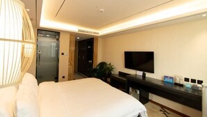 A hotel room with a bed, a TV, a desk with a computer, and a door leading to a bathroom. - Yuyang Hotel (Pinggu)