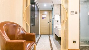 A hotel hallway with a leather armchair, a wooden door, a bathroom with a sink, and a patterned rug. - Yuyang Hotel (Pinggu)