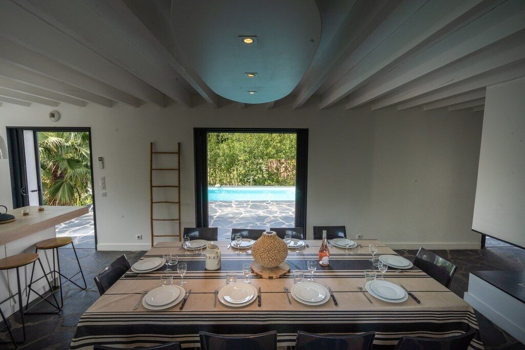 A dining area with a large table set for six, a view of a swimming pool, and a modern interior design.