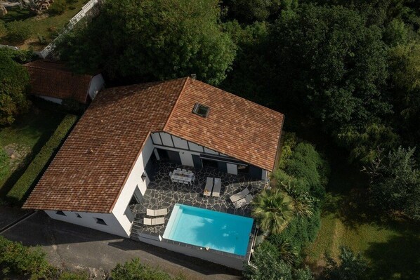 A modern house with a swimming pool, stone patio, and a tiled roof.