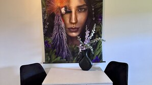 Ein Essbereich mit einem weißen Tisch und zwei schwarzen Stühlen, einer Wanddekoration mit floralen und Vogelmotiven sowie einer Pendelleuchte.