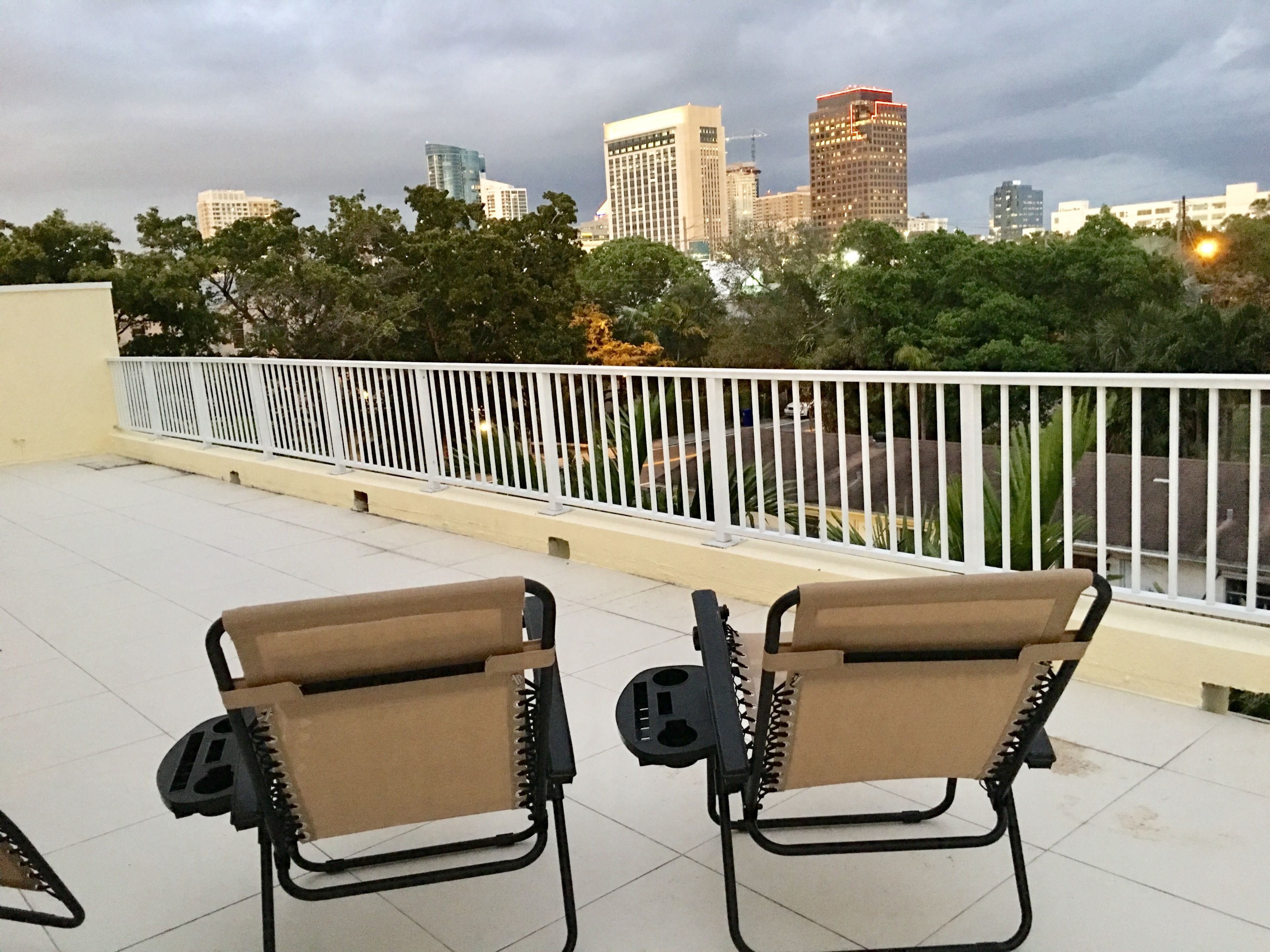 Two foldable chairs on a balcony with a city skyline in the background.
