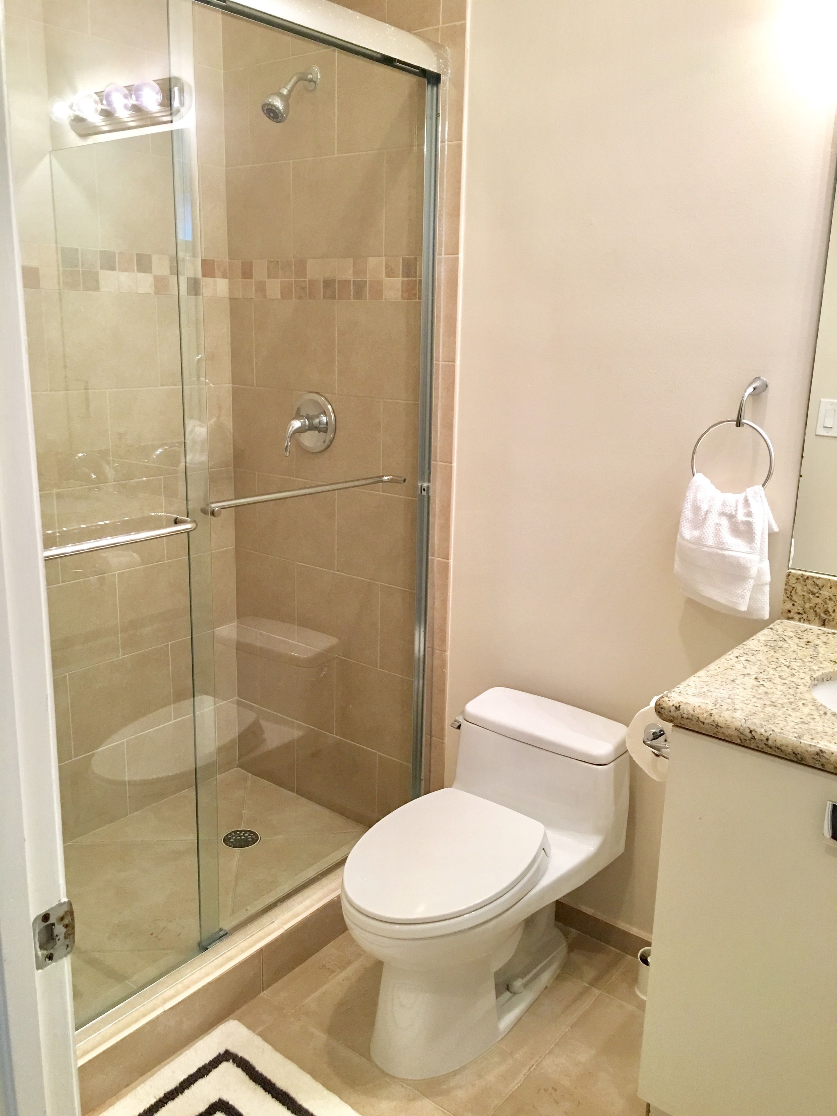 A bathroom with a glass-enclosed shower, a toilet, and a sink with a granite countertop.