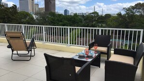 A balcony with outdoor furniture, a table with a bowl and wine glasses, and a view of city buildings and greenery. - 4BR Townhouse 320 by Ideal Experience VR (Fort Lauderdale)