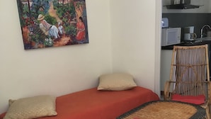 A room with a bed, a wicker chair, a small table, and a painting on the wall.