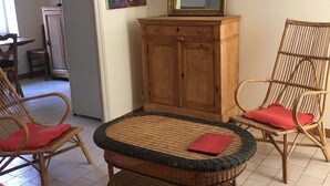 A room with a wicker round table, two wicker chairs, a wooden cabinet, and a mirror on the wall.