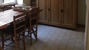 A dining area with a wooden table and chairs, a cabinet with kitchenware, and a painting on the wall.