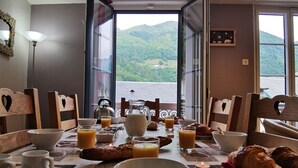 A breakfast table with croissants, orange juice, and a candle, overlooking a mountainous landscape.