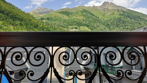 A balcony with a wrought iron railing overlooking a mountainous landscape with lush greenery and a clear sky.