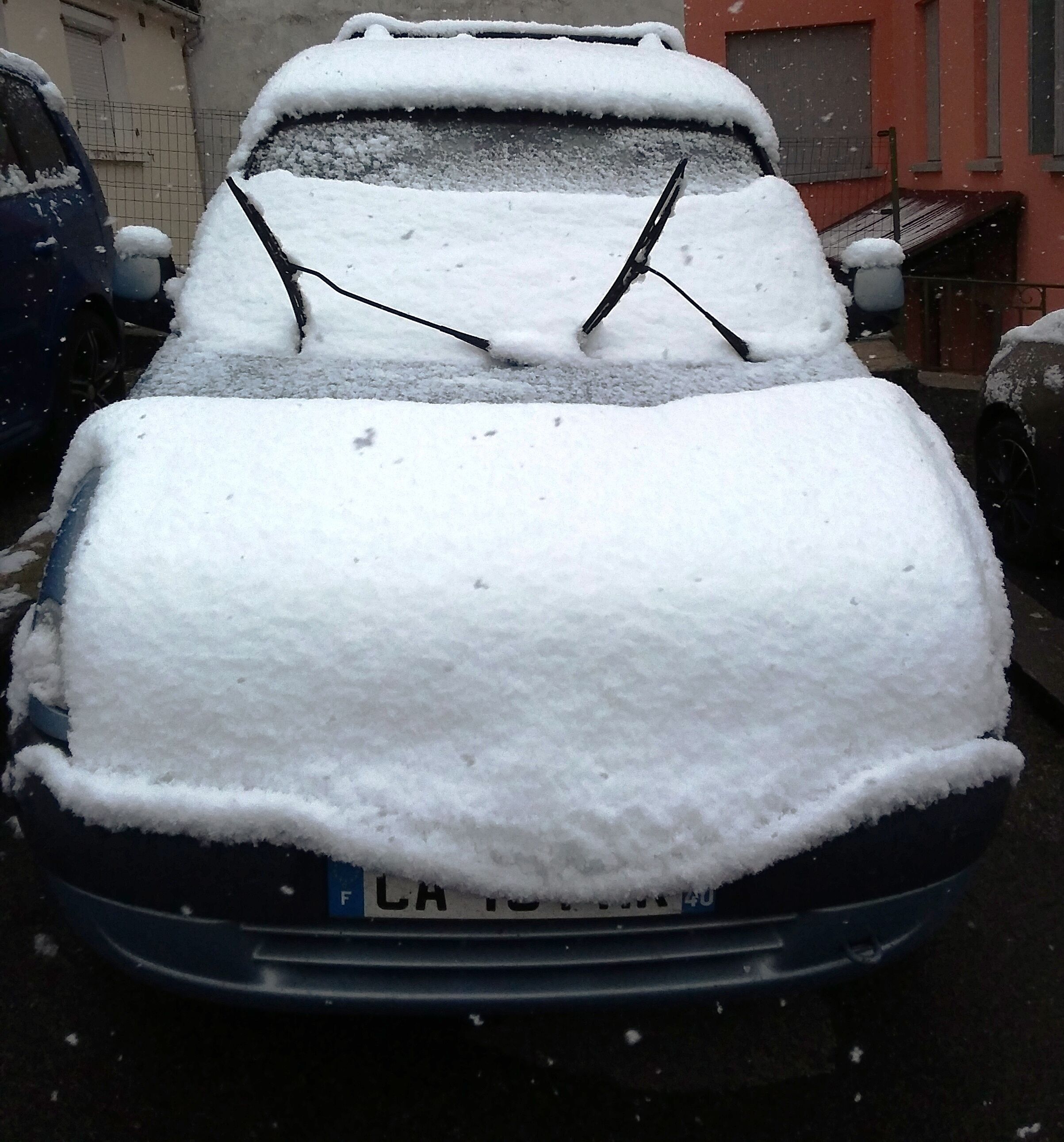 A car covered in snow with a visible license plate.