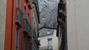 A narrow street with buildings on either side, featuring balconies and a snowy mountain in the background.