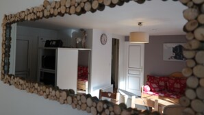 A room with a mirror framed by wooden logs, a bed with red bedding, a wooden chair, and a wooden table.