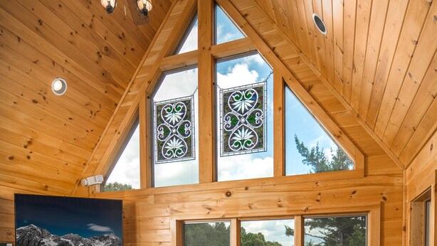 A cozy cabin interior with a stone fireplace, leather sofa, and large windows offering a view of the outdoors.
