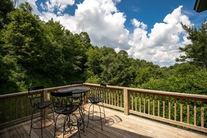 A wooden deck with a table and chairs, surrounded by lush greenery and a wooden railing.