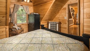 A cozy wooden cabin bedroom with a bed, a dresser, a chair, and a ceiling fan.