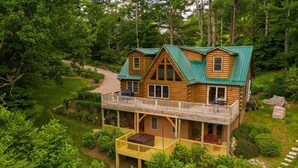 A log cabin with a balcony and a deck, surrounded by lush greenery.