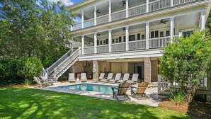 A two-story building with a swimming pool, outdoor seating, and a staircase leading to the upper level. - Luxury 2nd Row Home, Chefs Kitchen, Pool, Free Golf, Great for Entertaining (Hilton Head)