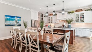 A modern kitchen with white cabinetry, a wooden dining table, and pendant lighting. - Luxury 2nd Row Home, Chefs Kitchen, Pool, Free Golf, Great for Entertaining (Hilton Head)